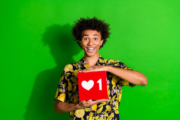 照片中开朗有趣的男人穿着时髦的热带印花衣服，手拿红牌孤立在绿色背景上图片下载