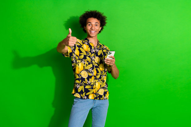 照片积极的酷男人穿着时髦的热带印花衣服大拇指向上孤立在绿色背景图片下载