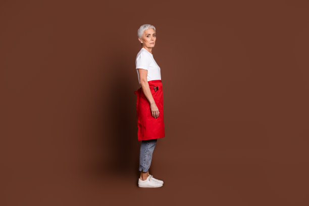 可爱的养老金领取者女士美发师工作理发店站侧面穿着统一的棕色背景孤立的照片图片下载