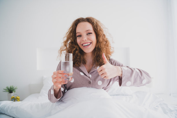 照片漂亮的年轻女孩水杯拇指向上穿睡衣明亮的室内卧室公寓室内图片下载