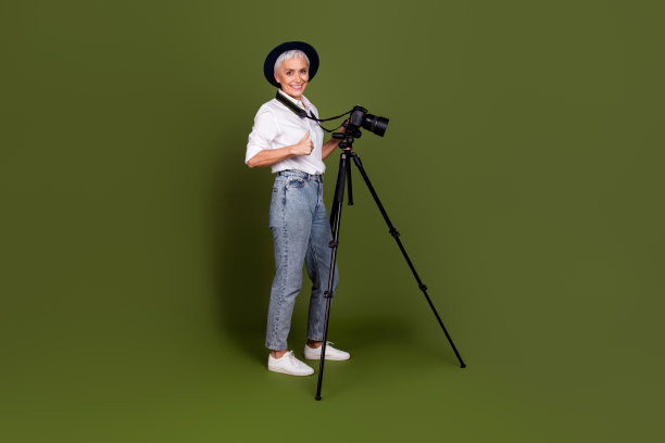 可爱自信的女摄影师全身照片，戴着白色衬衫帽子，拇指向上，拍摄视频孤立的绿色背景图片下载