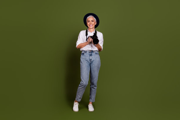 全身照片微笑迷人的女摄影师穿着白色衬衫帽拿相机孤立卡其色背景图片下载