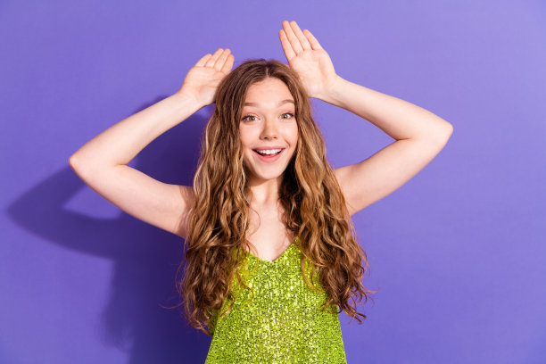 漂亮的十几岁女孩的照片肖像显示兔子耳朵的手势穿着时髦的绿色服装孤立的紫色背景图片下载