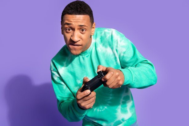 照片中时髦酷的家伙穿着绿松石色的运动衫享受着ps游戏的空旷空间，孤立的紫罗兰色背景图片下载