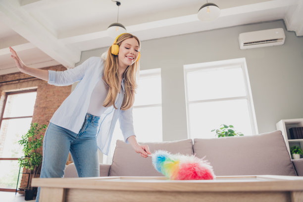 照片中闪亮可爱的女孩穿着休闲衬衫，微笑着听着音乐在室内房子公寓房间里消毒图片下载