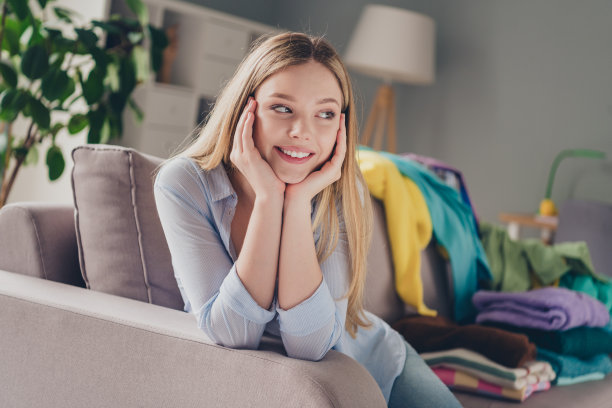 照片的积极梦想的女孩穿着蓝色衬衫微笑打包衣服在室内的房子公寓房间图片下载