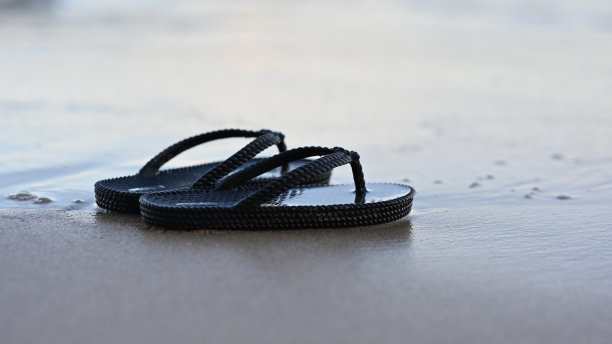 沙滩上的人字拖特写图片，热带沙滩上的凉鞋，放松旅行度假的概念图片下载