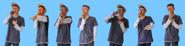 年轻富有表现力的歌手，快乐的男人，穿着灰色t恤，戴着眼镜和帽子，对着麦克风张开双手唱歌，在朴素的浅蓝色背景的工作室里。收集或汇编。图片下载