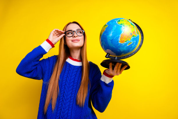 美丽的年轻女孩抱着地球地理老师的照片肖像，穿着时髦的蓝色针织衫，孤立在黄色背景上图片下载