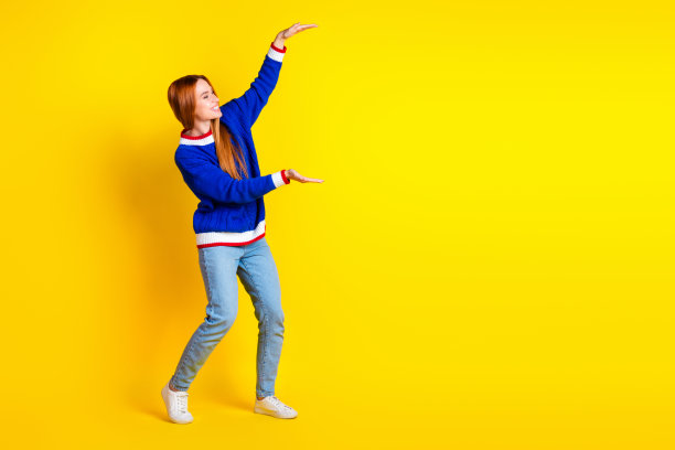 照片中的红发模特年轻开朗的女人穿着蓝色时髦的套头衫和牛仔裤，在黄色的背景上显得有些孤立图片下载