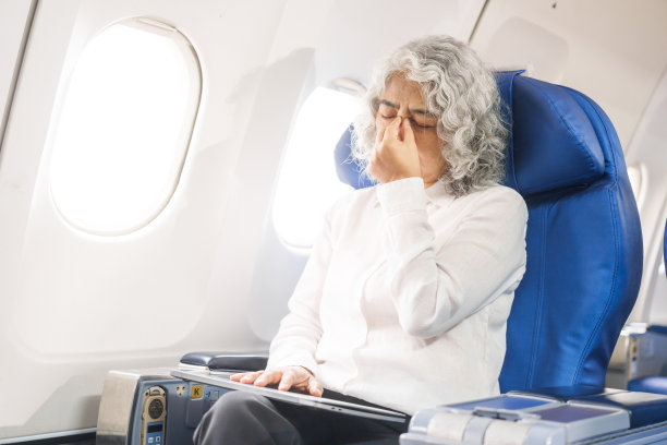 在一架出国旅行的客机上，一位成熟的女士坐在窗边。她看起来不太舒服，头痛、恶心和呕吐，这使她对旅行的兴奋感大打折扣。图片下载