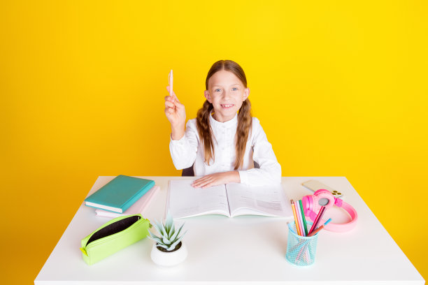 照片肖像可爱的小女生做作业，坐在桌子上穿着时尚的制服孤立在黄色的背景图片下载