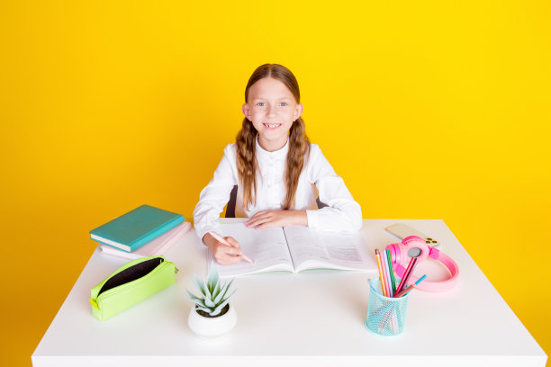 可爱的小女生写作业的照片肖像穿着时尚的制服孤立在黄色的背景图片下载