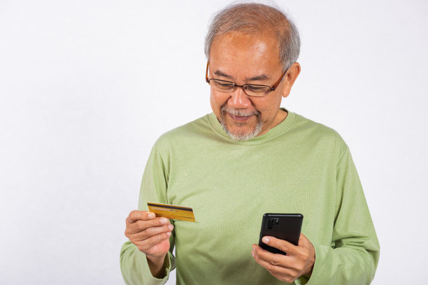 亚洲面带微笑的老人手里拿着信用卡和手机。他很可能是在检查他的银行账户余额，或者是在单独拍摄一张摄影照片图片下载
