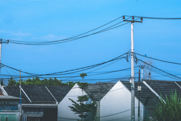 位于印度尼西亚的一排带有屋顶瓦片和电线杆元件的房子的照片。房子的瓦片照在晴朗的天空上图片下载