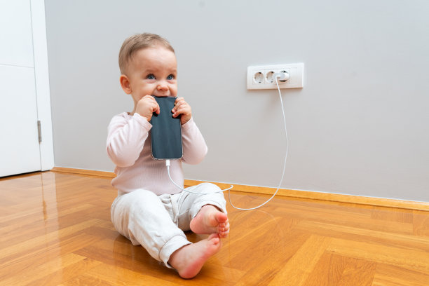 小孩咬正在充电的手机。日常危险的概念图片下载