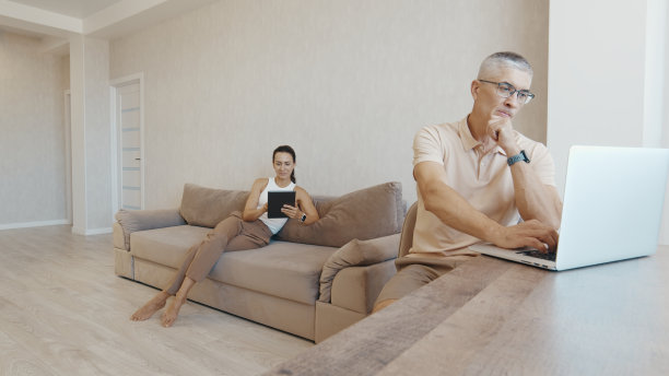 夫妇在时尚的客厅里用笔记本电脑和平板电脑放松图片下载