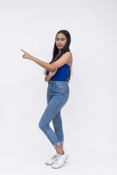 一个年轻漂亮的亚洲女人指着左边。全身照片被隔离在白色背景上。图片下载