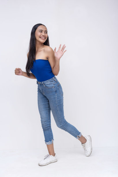 一位走在路上的年轻菲律宾女子回头看了看，愉快地挥手致意。全身照片，孤立在白色背景上。图片下载