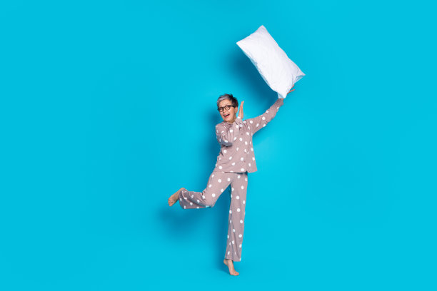 照片正面可爱的高级妇女穿着时髦的睡衣捕捉柔软的枕头孤立的蓝色背景图片下载