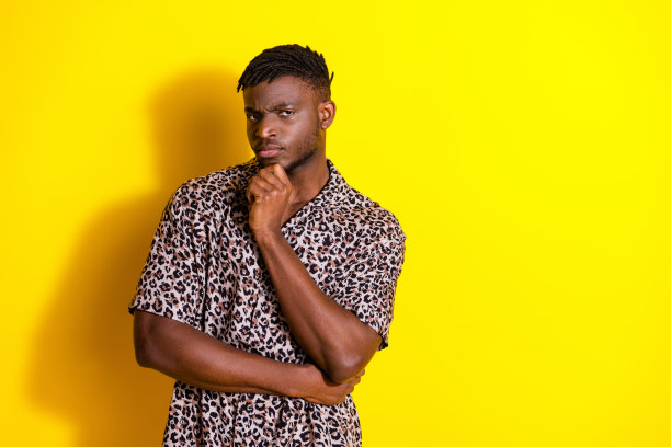 照片中，严肃帅气的男人穿着时尚的衣服，触摸着脸，孤立在黄色的背景上图片下载