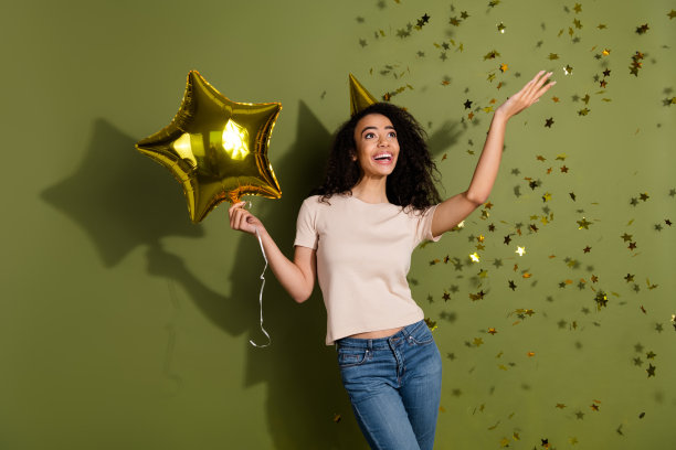 照片中可爱的女孩穿着米色t恤，手拿气球，在卡其色的背景下，看着空旷的太空中飞行的星星图片下载