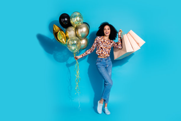 照片中快乐的女人穿着时髦的衣服，拿着气球，在蓝色的背景上单独销售图片下载