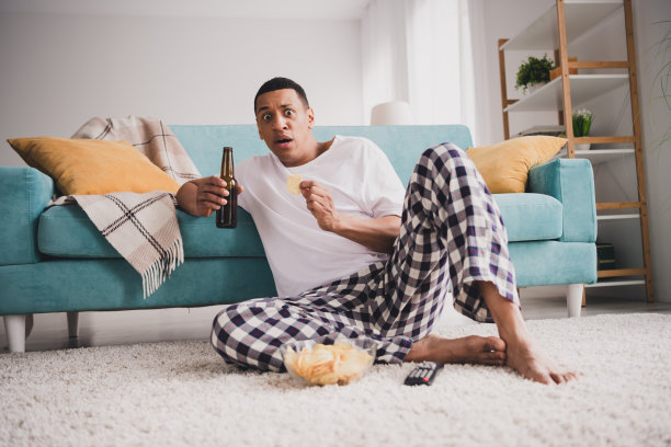 照片震惊有趣的家伙睡衣睡衣看足球享受周末沙发喝酒在室内房间家里房子图片下载