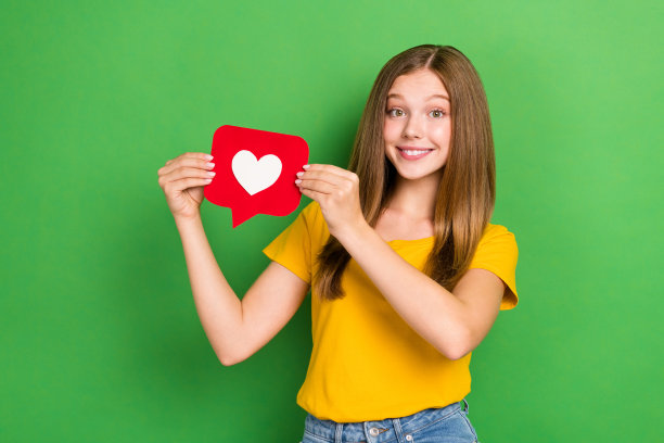 青少年照片可爱的女学生女士拿着红纸形状的心形符号，就像订阅新频道一样，孤立在绿色的背景上图片下载