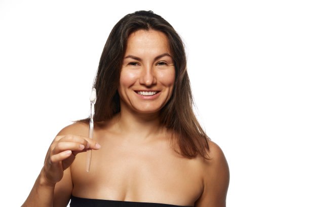 深色头发的女人带着充满活力的微笑看着照相机拿着牙刷，背景是白色的工作室。图片下载