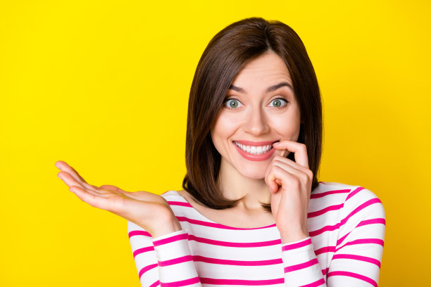 漂亮的年轻女士的照片肖像微笑咬指甲购物提供手掌穿着时尚的条纹服装孤立的黄色背景图片下载