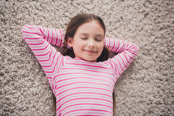 照片中可爱可爱的女孩女儿躺在地板柔软的地毯上睡觉，手放在脑后，从家里在室内教育图片下载