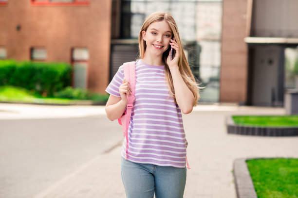 照片积极的好心情的女孩穿着紫色的t恤背包谈论现代小工具走在城市户外的城市小镇图片下载