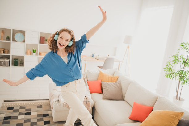 欢快的年轻女性的照片耳机跳舞摊开双手蓝色衬衫享受周末在室内买新公寓在房子里的家图片下载