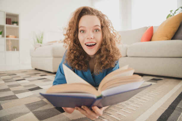 有吸引力的时尚年轻女子躺在地板上的全身照片读书惊奇的蓝色衬衫移动新公寓的家室内室内图片下载