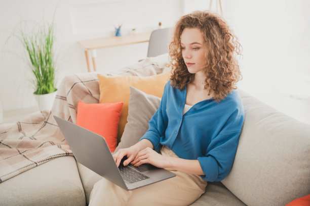 快乐的年轻女孩的照片，坐在沙发上网本电子商务蓝色衬衫享受生活的新公寓房间，光的房子，平的室内图片下载