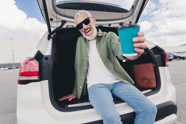 时髦酷的成熟男人穿着休闲衬衫坐在汽车后备箱分享你的咖啡去户外城市停车场的照片图片下载