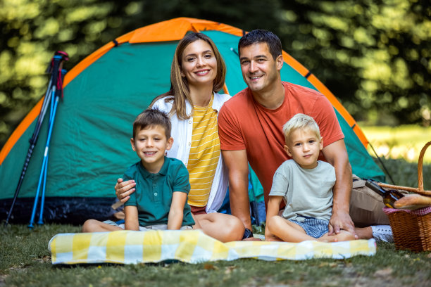 一张幸福的四口之家在森林里野营时坐在帐篷前的照片。图片下载