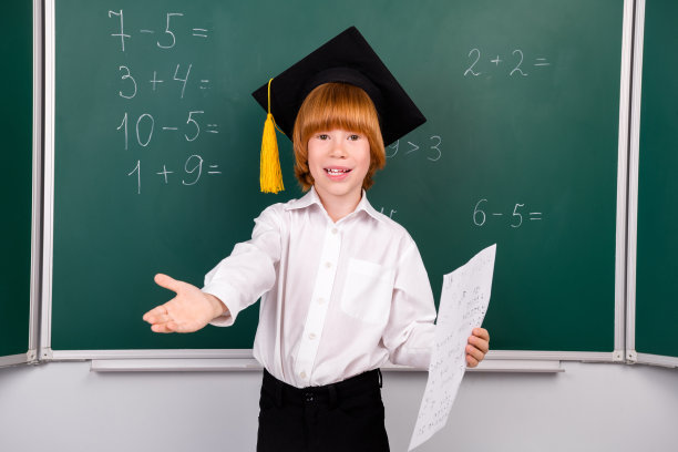 照片中可爱的小男生毕业戴帽子教课穿着时髦的校服教室黑板背景图片下载