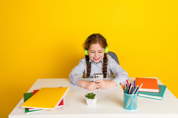 照片中的小女生桌面耳机智能手机戴统一孤立的黄色背景图片下载