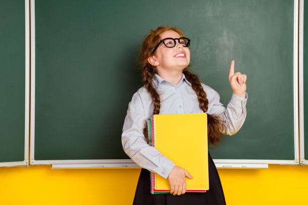 小女生的照片，书中手指指向空的空间，穿着校服孤立在黄色黑板背景上图片下载