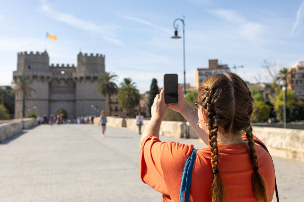 在欧洲旅行，穿着休闲装的红发女游客用智能手机给托雷斯·德·塞拉诺斯塔拍照。迷人的女游客正在探索新的城市。高质量的照片，后视图图片下载