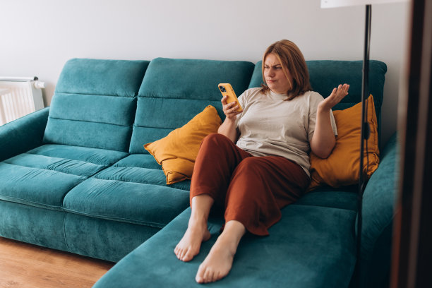 沮丧、悲伤、怀疑、严肃的女人拿着智能手机在室内交流。消极的人情绪，沉思的女孩坐在家里。红发女人拿着智能手机。尖叫，憎恨，愤怒图片下载