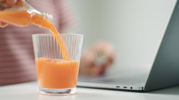 一个在家工作的女人在往杯子里倒果汁。图片下载