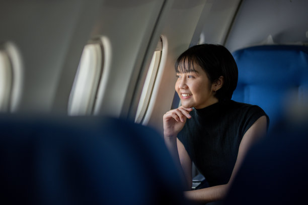 一位心情愉快的女士坐在飞机靠窗的座位上欣赏窗外的景色，她微笑着望着窗外。图片下载
