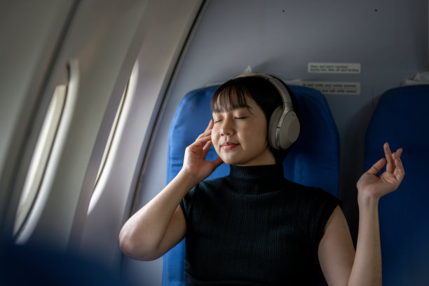 乘客坐在飞机座位上，戴着耳机享受着宁静放松的音乐。图片下载