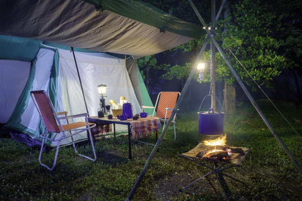 夜晚的露营帐篷，复古的小屋帐篷，古董灯笼，复古的椅子，以及森林里木制桌子上的户外咖啡制作设备图片下载