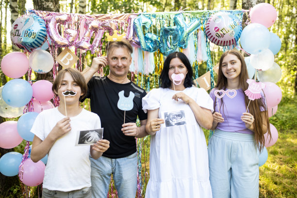 有两个孩子的家庭在性别揭秘派对上。拿着配件、道具、纸胡子和超声波图片。关注父母。图片下载