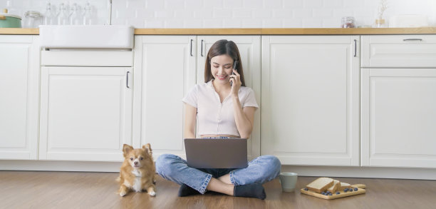 亚洲书呆子眼镜女人工作与电脑手机在地板上与她的宠物狗。咖啡面包休息时间。中小企业的网上办公技术。周末在家工作。图片下载