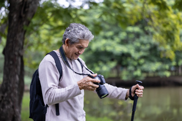 亚洲老人在森林中徒步旅行，同时用相机拍摄难忘的照片，为老年人户外锻炼和自然环境治疗理念图片下载